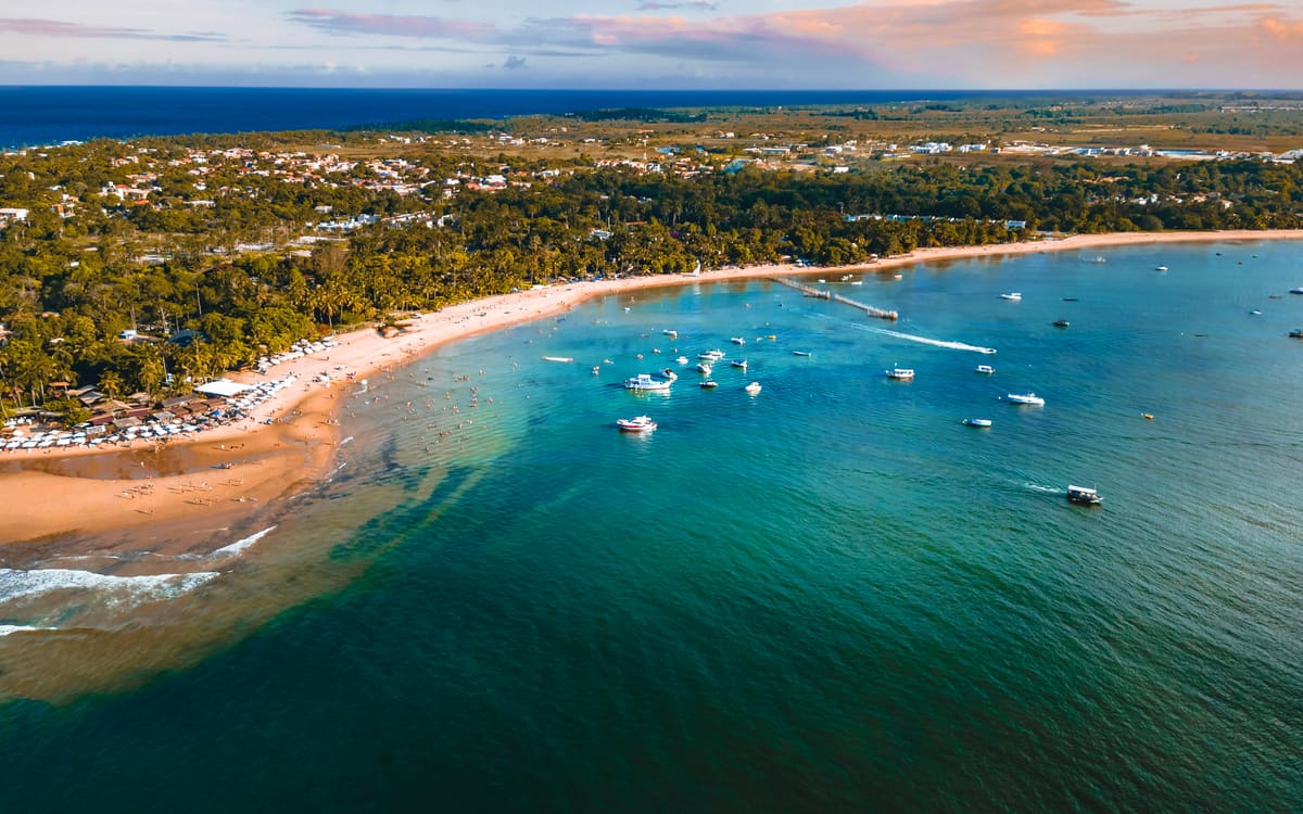Vista aérea da enseada de Barra Grande com o píer e barcos ancorados na água azul.